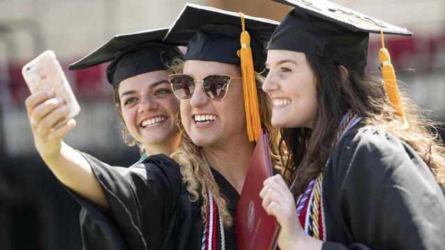 three graduates in graduate caps and gowns taking selfie